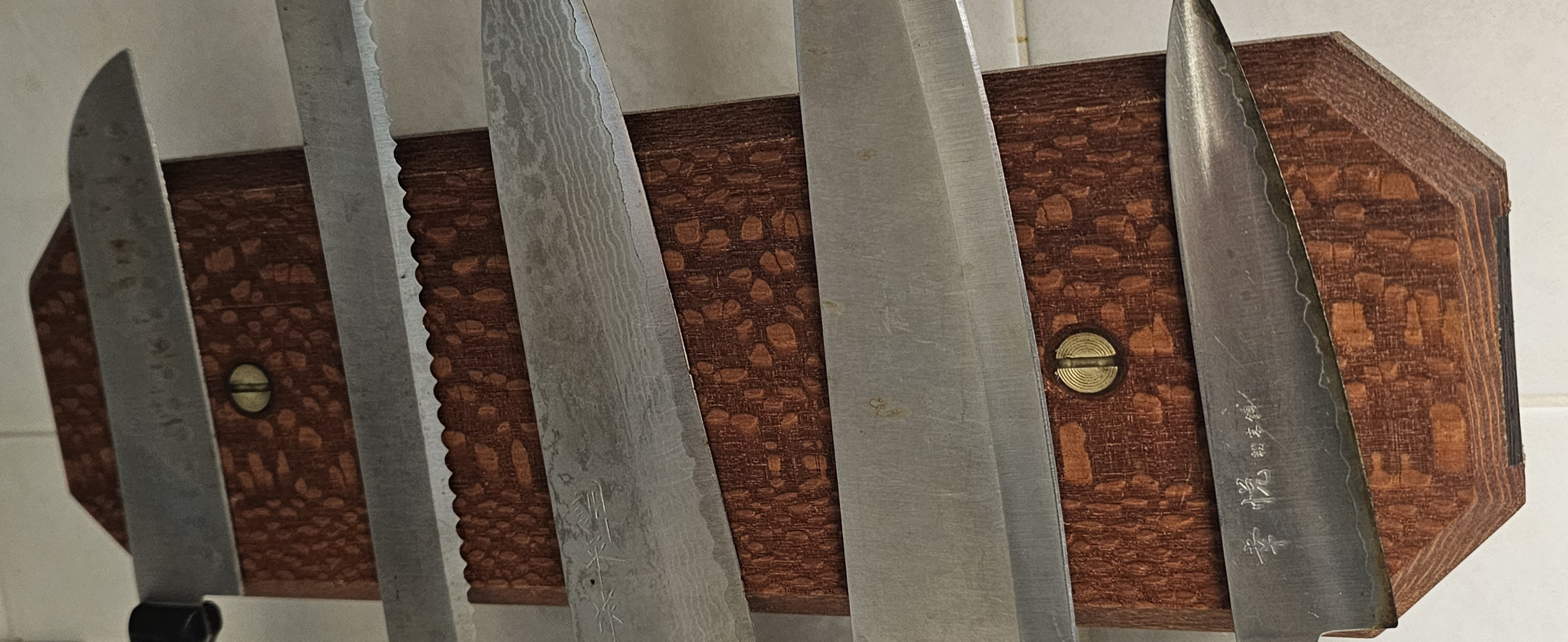 Wall-mounted magnetic knife holder made of leopardwood, mounted on a kitchen wall, holding multiple kitchen knives.