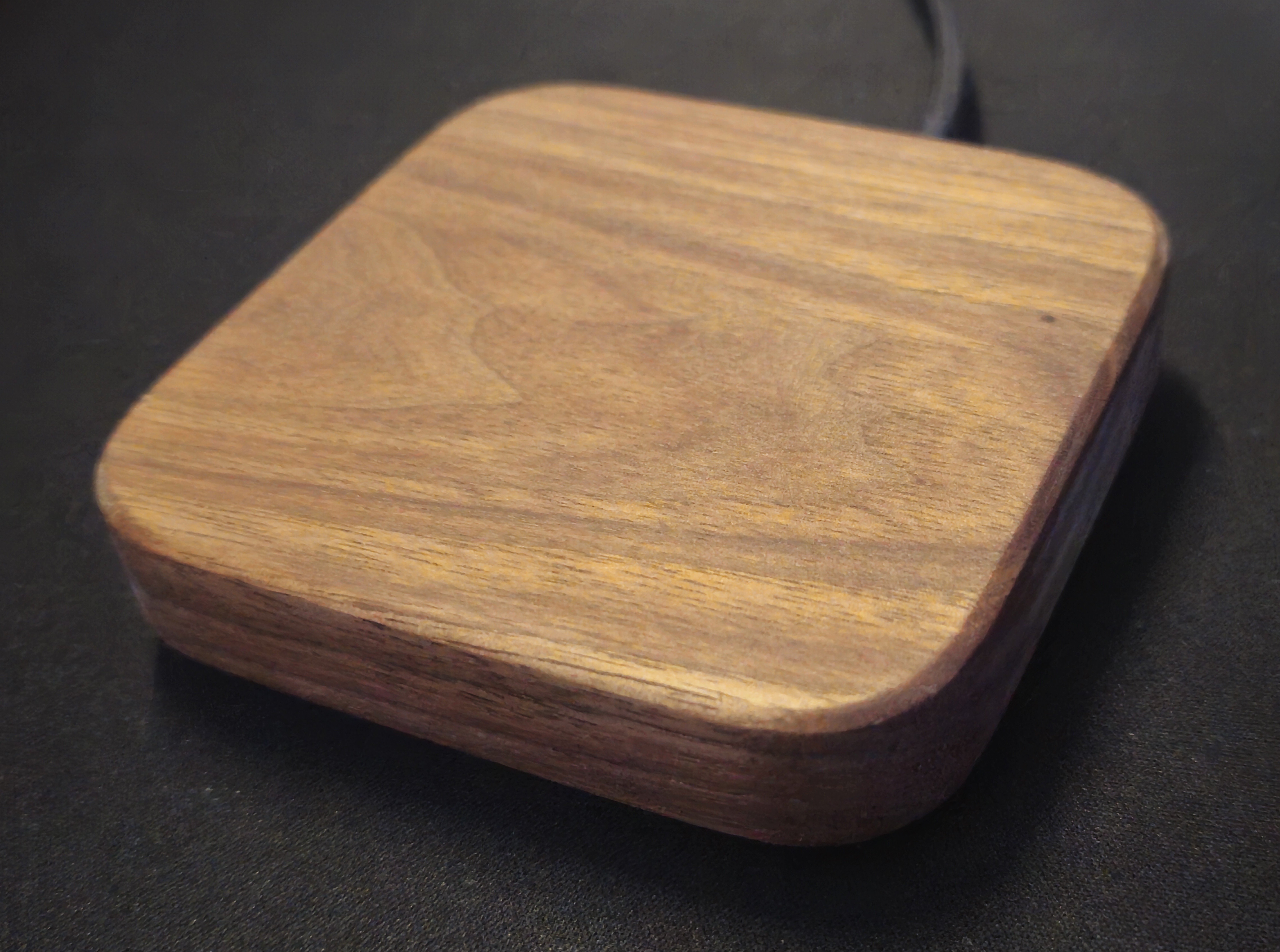 Square wireless charger in solid walnut with rounded corners, USB cable entering the side