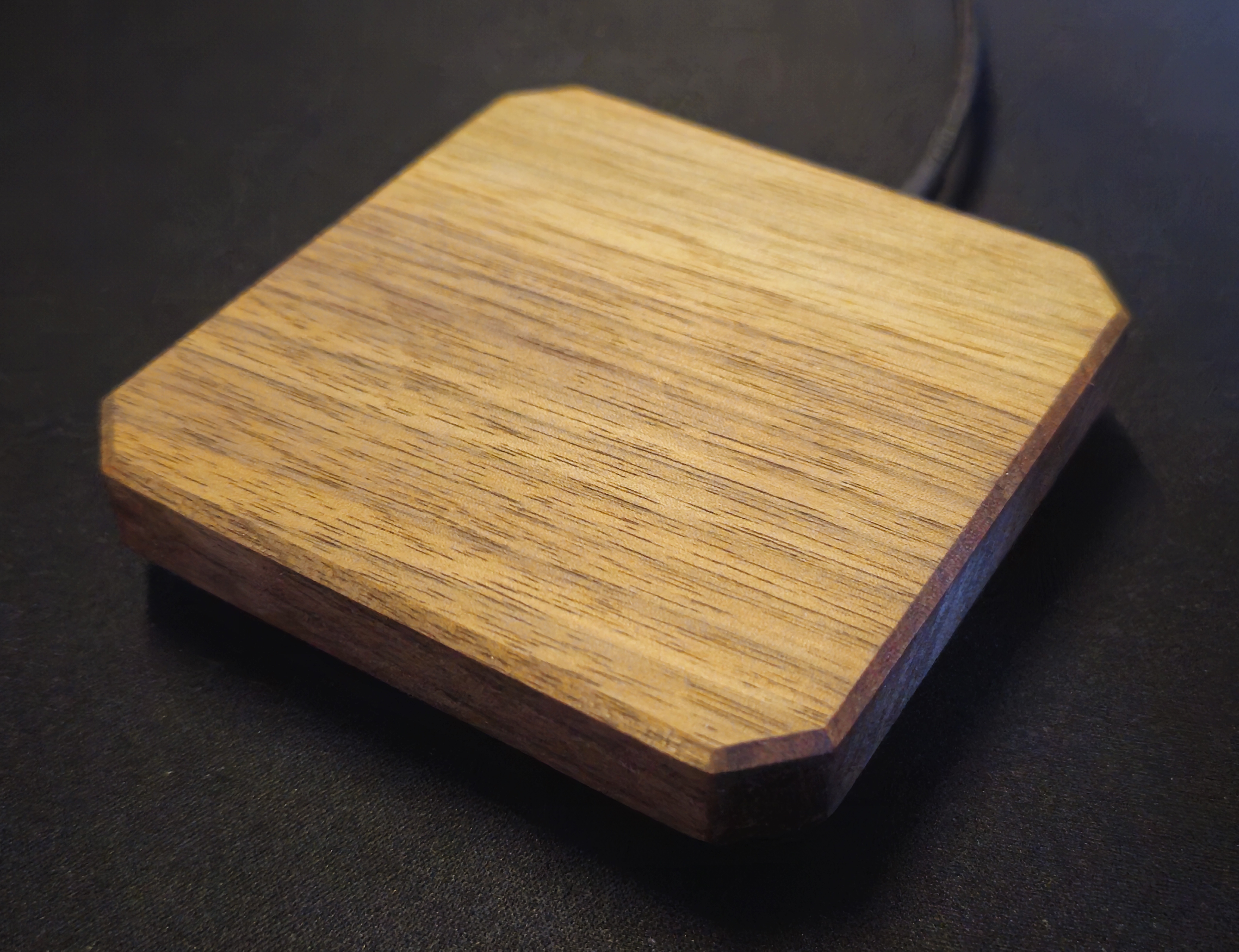 Square wireless charger in solid walnut with cut corners, USB cable entering the side